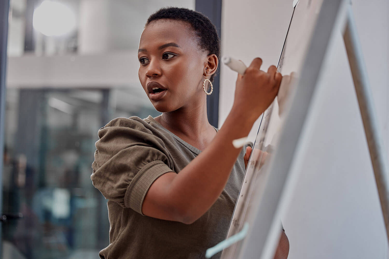 A woman with short cropped hair writes on a whiteboard