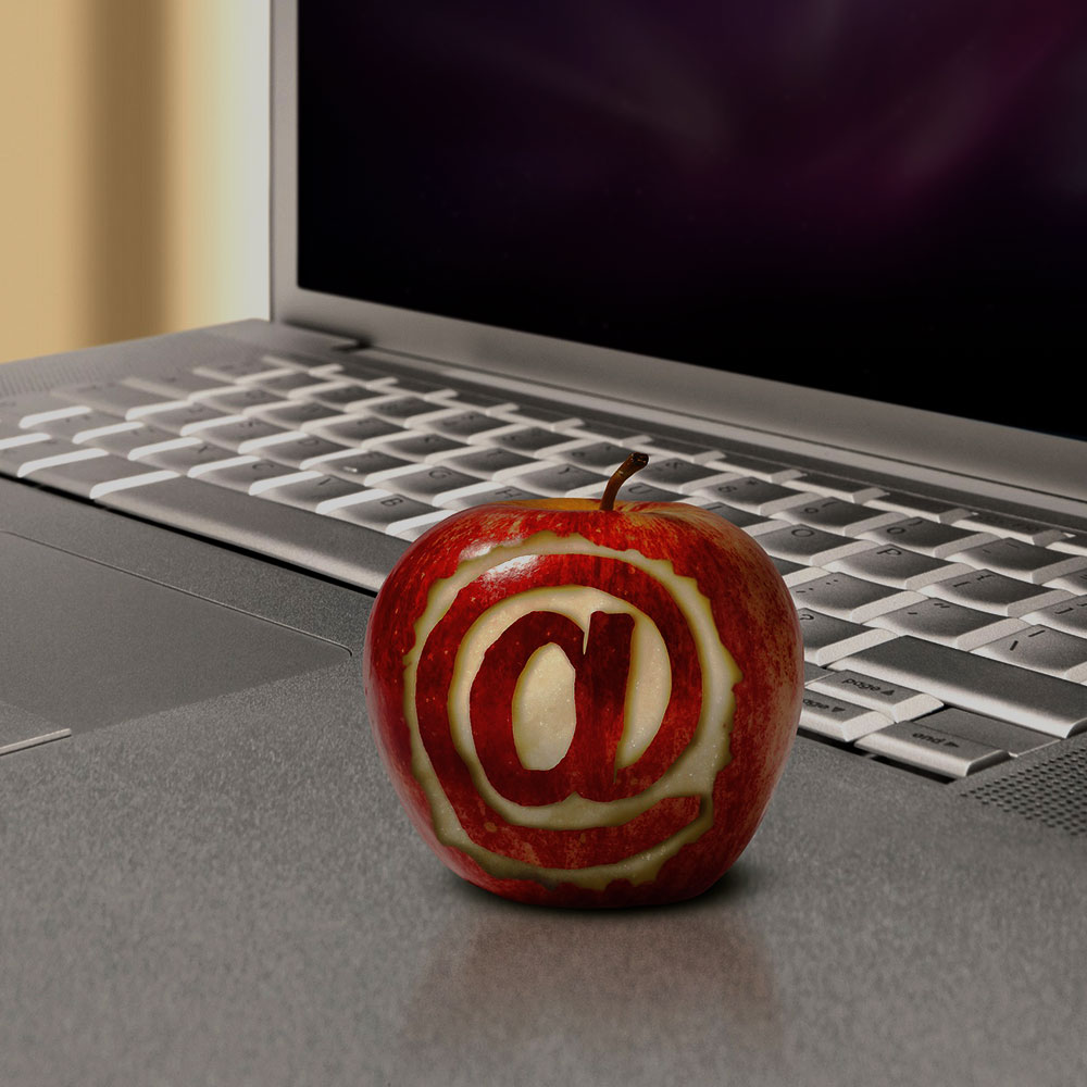 Apple with an 'at' symbol carved into it with laptop in the background