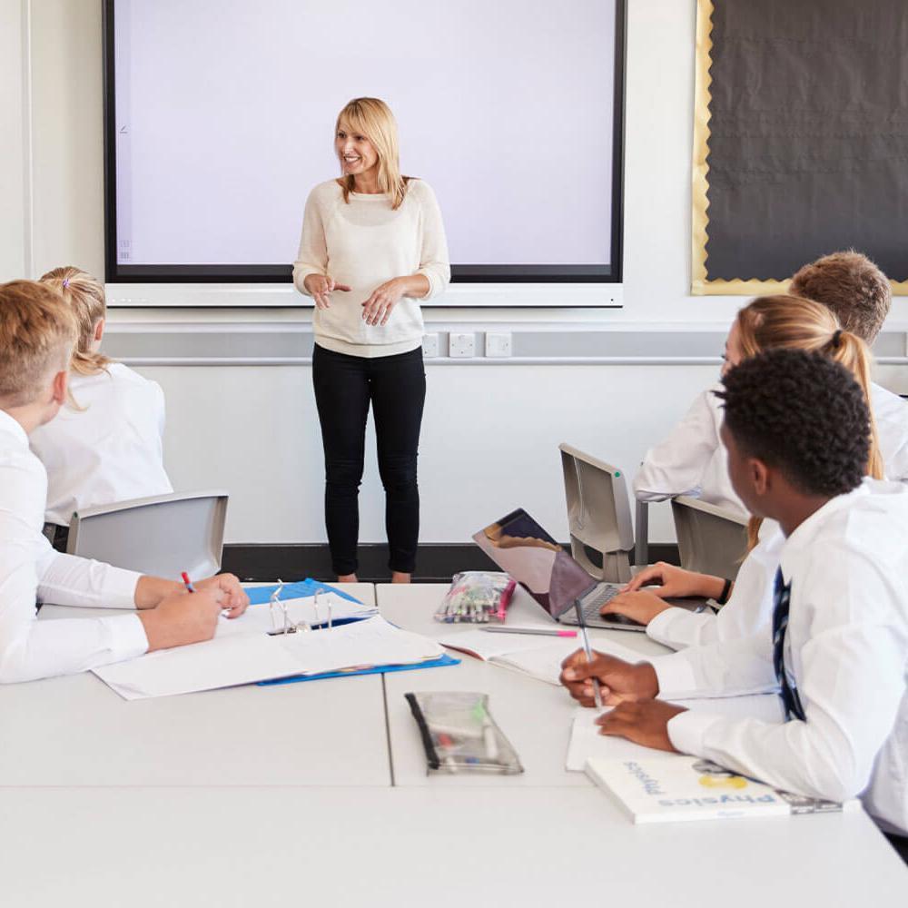 Teacher standing next to interactive whiteboard and teaching lesson to pupils