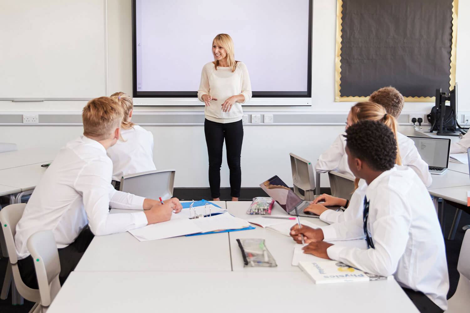 Teacher standing next to interactive whiteboard and teaching lesson to pupils