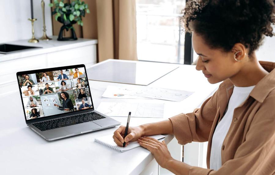 Woman takes notes on paper while attending a webinar using her laptop