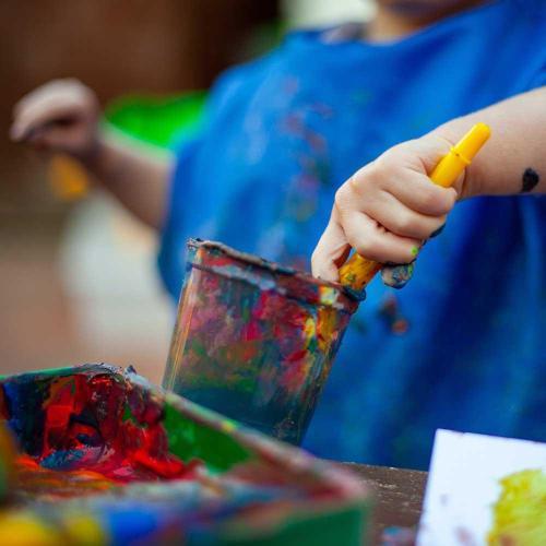 A young child wearing a blue apron experiments with mixing different paint colours