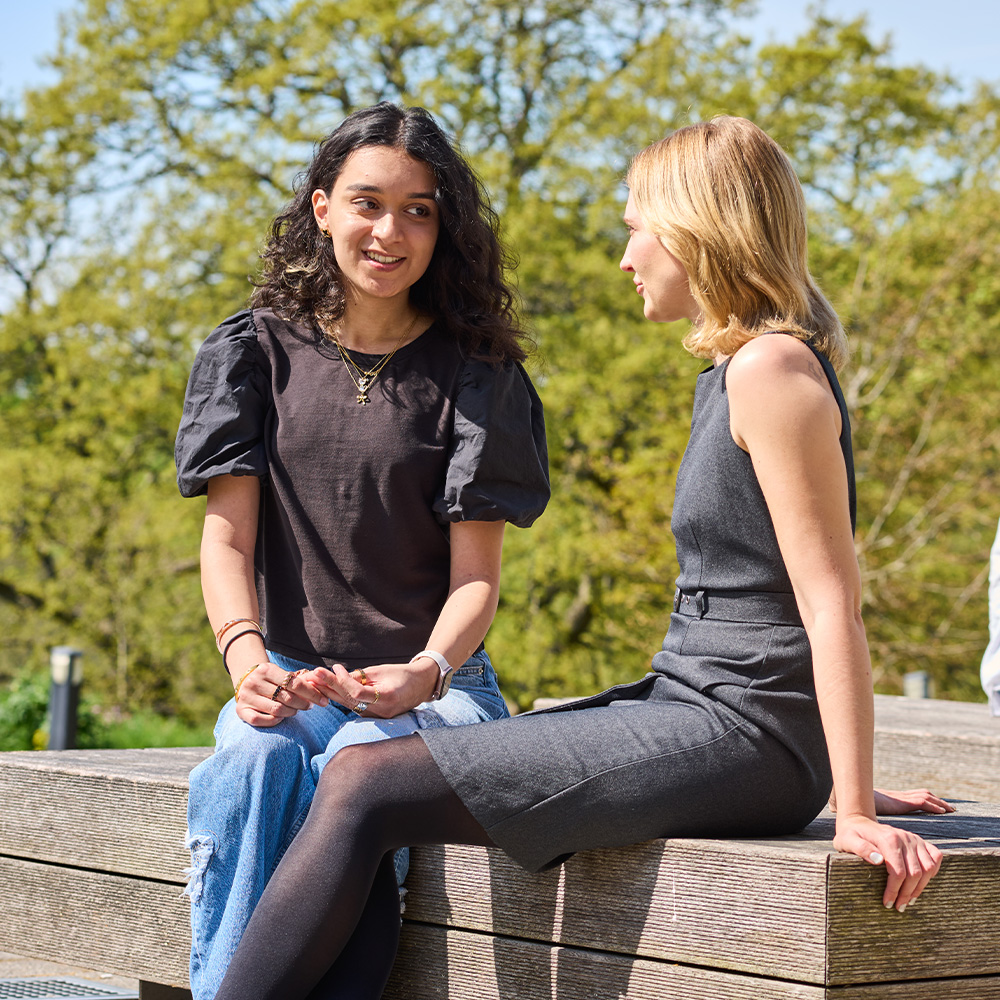 Two students talking whilst seated on a bench on campus