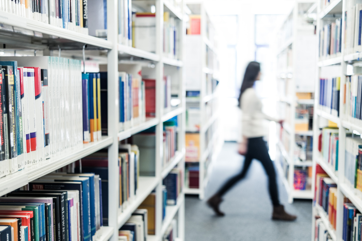 Shelves of books with blurred figure walking across aisle