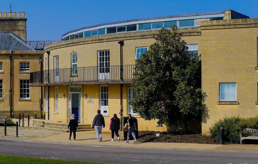 Students walking past a large tree into the curved front of a building