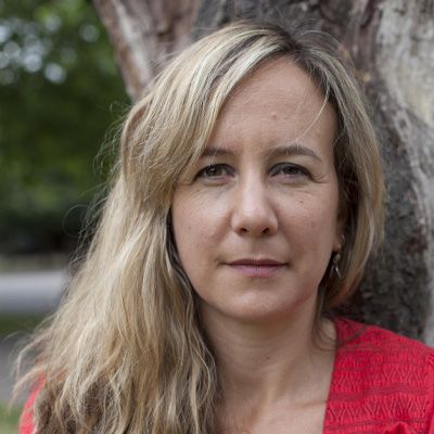 Person with long blonde hair in a red top in front of a tree