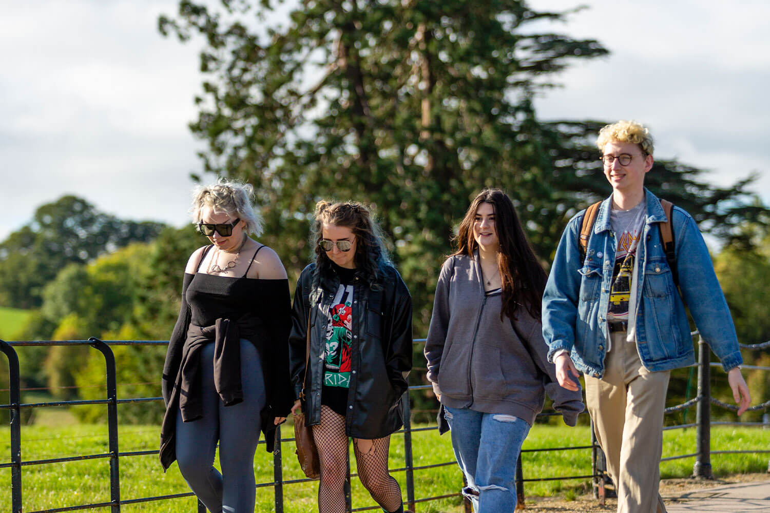 Four students walking on campus with mature trees in background