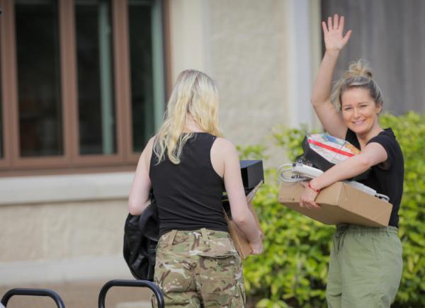 a woman waving as she carries boxes into a house