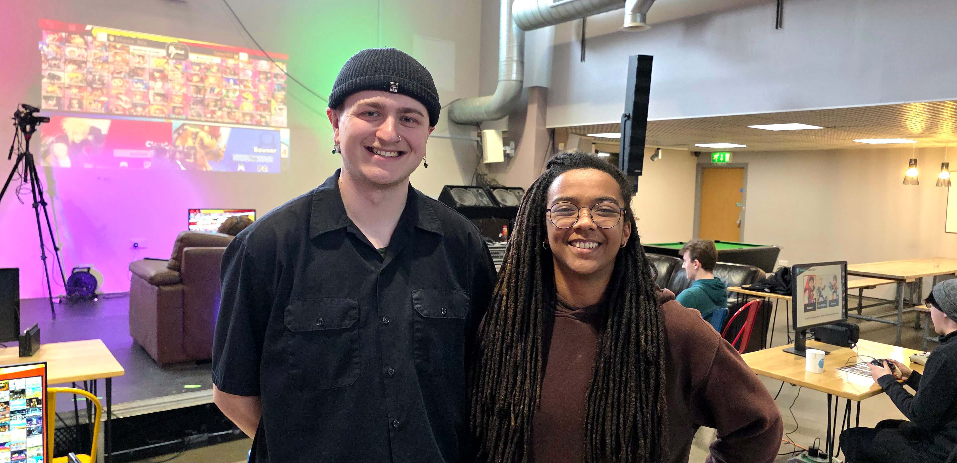 two people posing for the camera in front a large projector showcasing Super Smash Bros.