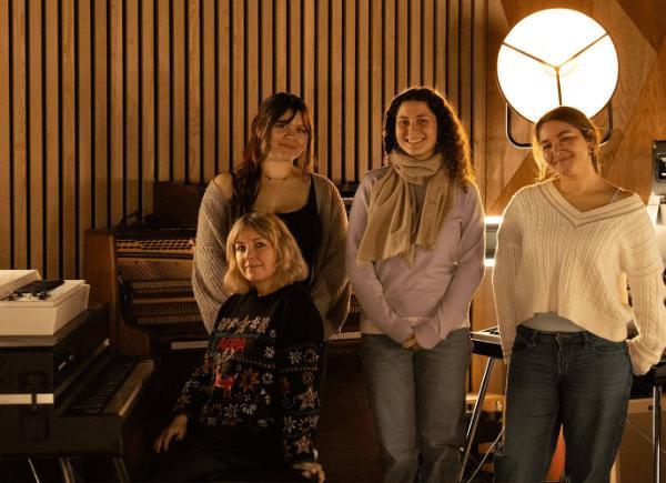A professor and three of her students gather around a piano