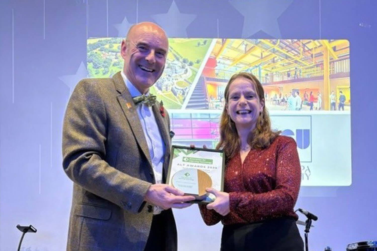 Two people stand on a stage, holding an award and certificate, in front of a BSU branded image on a backlit screen.