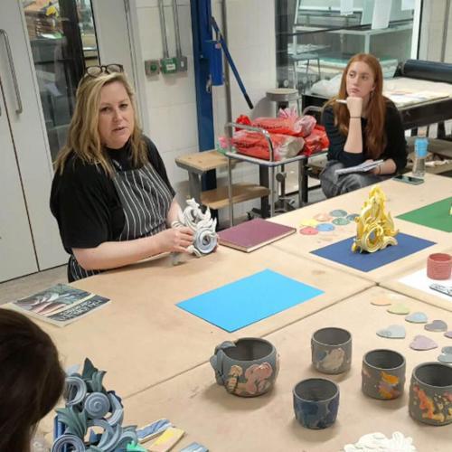 A group of students sit at a table to learn from a professional ceramicist