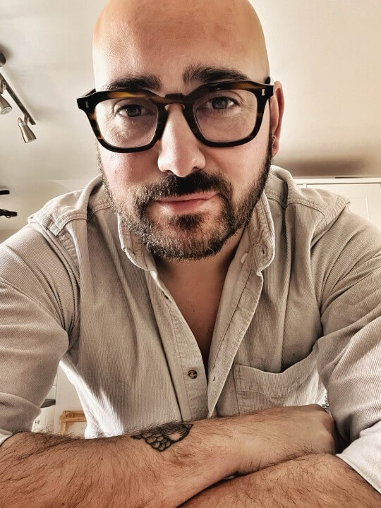 A headshot of writer Alex Farnham, wearing a grey buttoned shirt