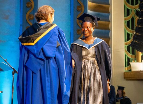 A smiling graduate shakes the Deputy Vice-Chacellor's hand on stage at the Forum