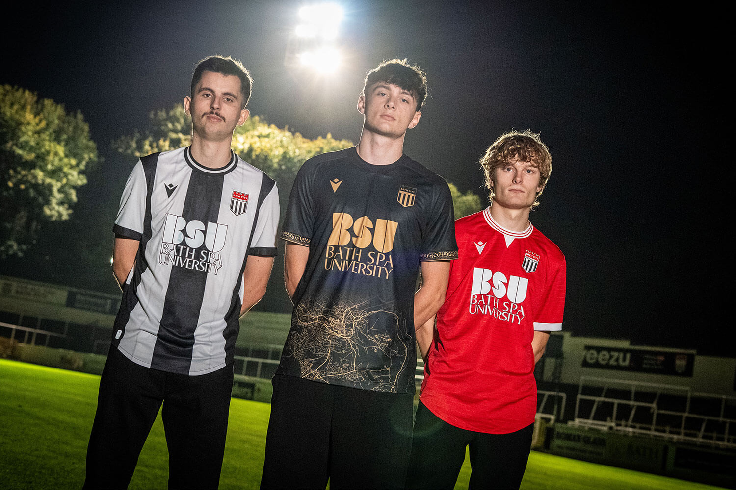 Three football shirts worn by three men in front of a large floodlight