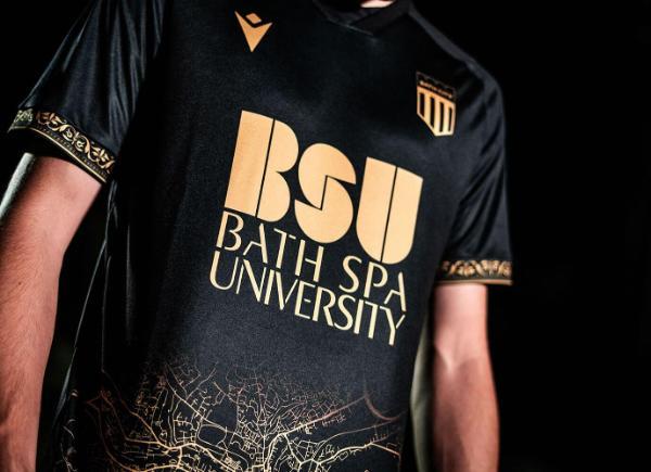 A black and gold football shirt with the Bath City FC logo and Bath Spa University logo emblazoned on the front