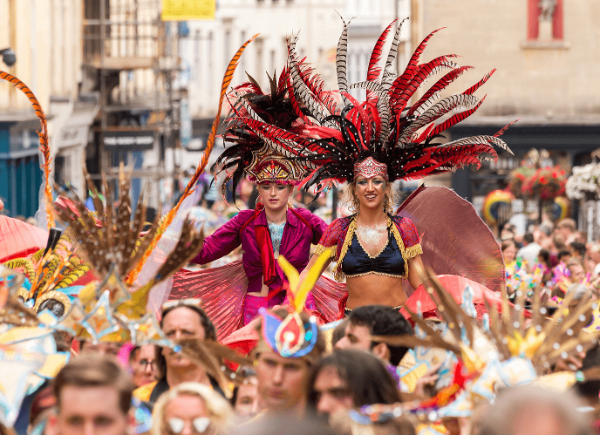 A crowd of people dressed in colourful carnival outfits walking through Bath