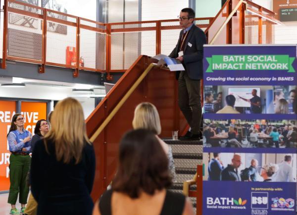 A person speaking at an event with a banner behind them