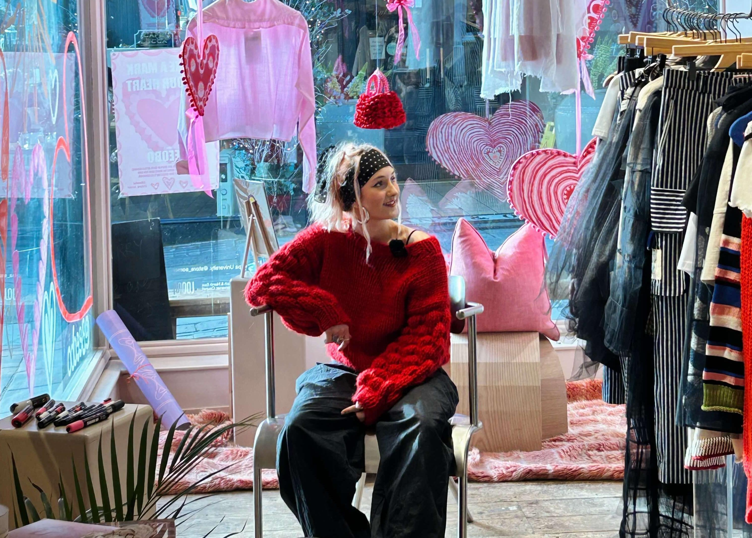 An artist sat on a chair in front of a Valentine's window display