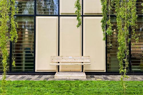 A wooden bench situated outside a large building with tress surrounding it