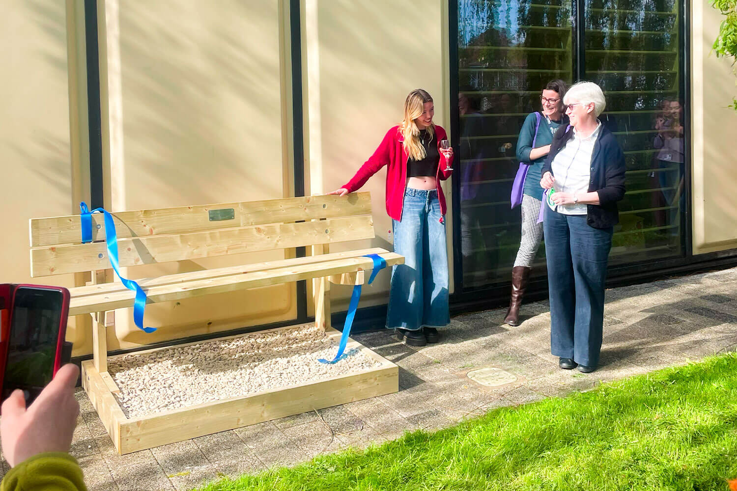 Three women looking at a wooden bench