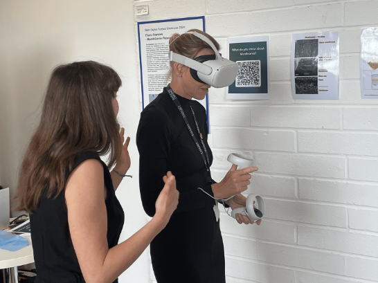 A woman wearing a VR headset is guided by another woman