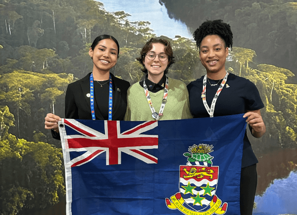 Three people stand smiling and holding a Cayman Islands flag