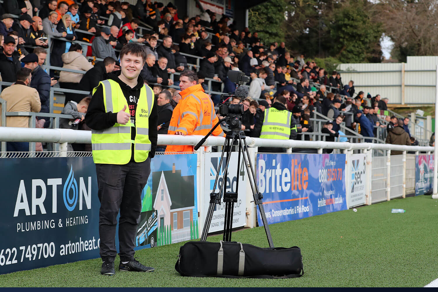 Bath City student Callum in a hi-vis jacket, pointing a camera in front of a large crowd