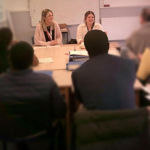 people sit around a desk in a classroom facing two BSU academics