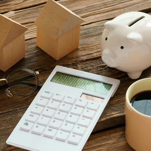 calculator, cup of coffee, piggy bank, wooden houses and glasses spread out on a wooden surface.