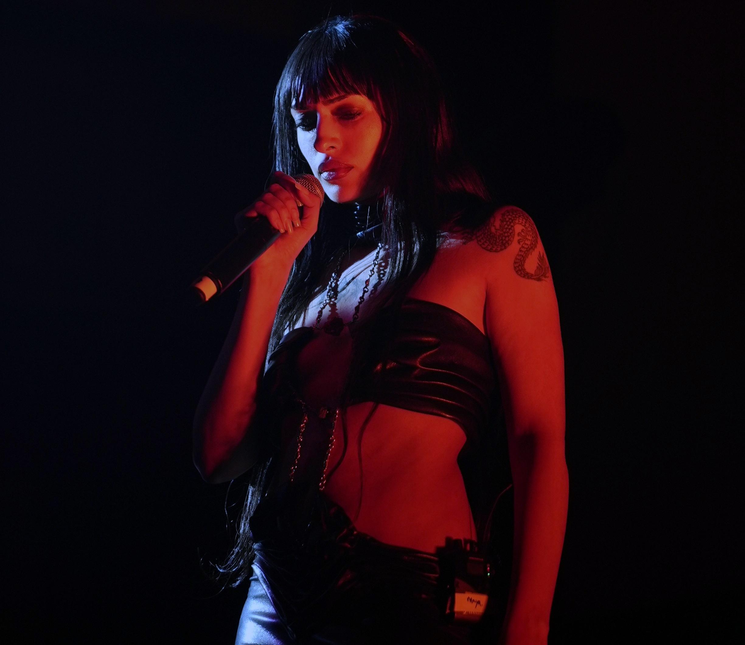 A woman on a dark stage sings with microphone in hand