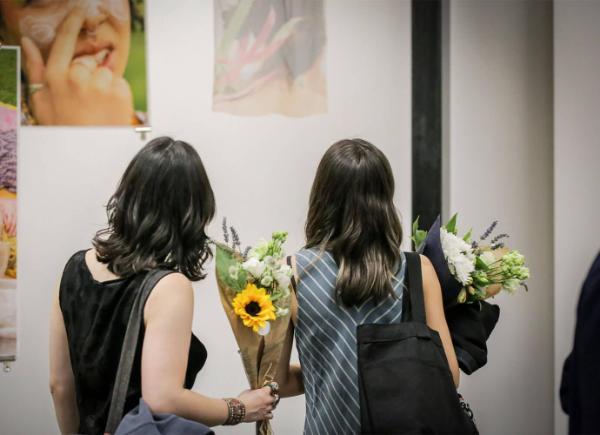 Two women with their backs to the camera, admiring artwork and holding flowers