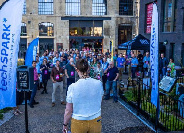 A group of people stand and listen to a speech outside