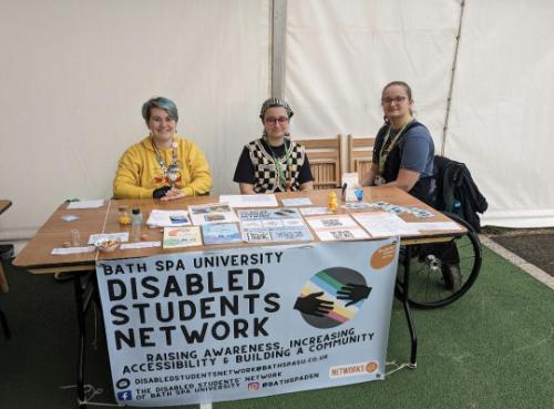 Three students sitting around a table with a banner advertising the Disabled Students Network