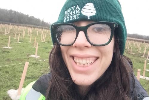 A smiling young woman wearing glasses and a green beanie hat