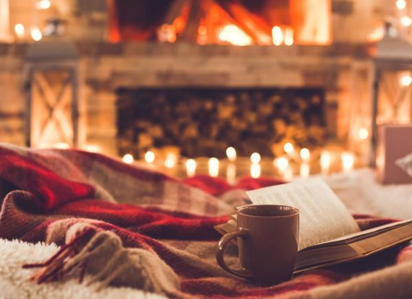 An open book next to a mug of tea in front of a fireplace