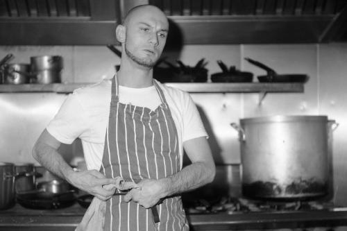 Black and white photo of Finlay Mills, tying on a chefs apron