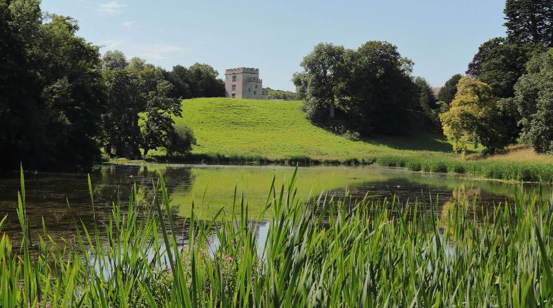 Newton Park lake with blue skies and the castle at the top of the hill