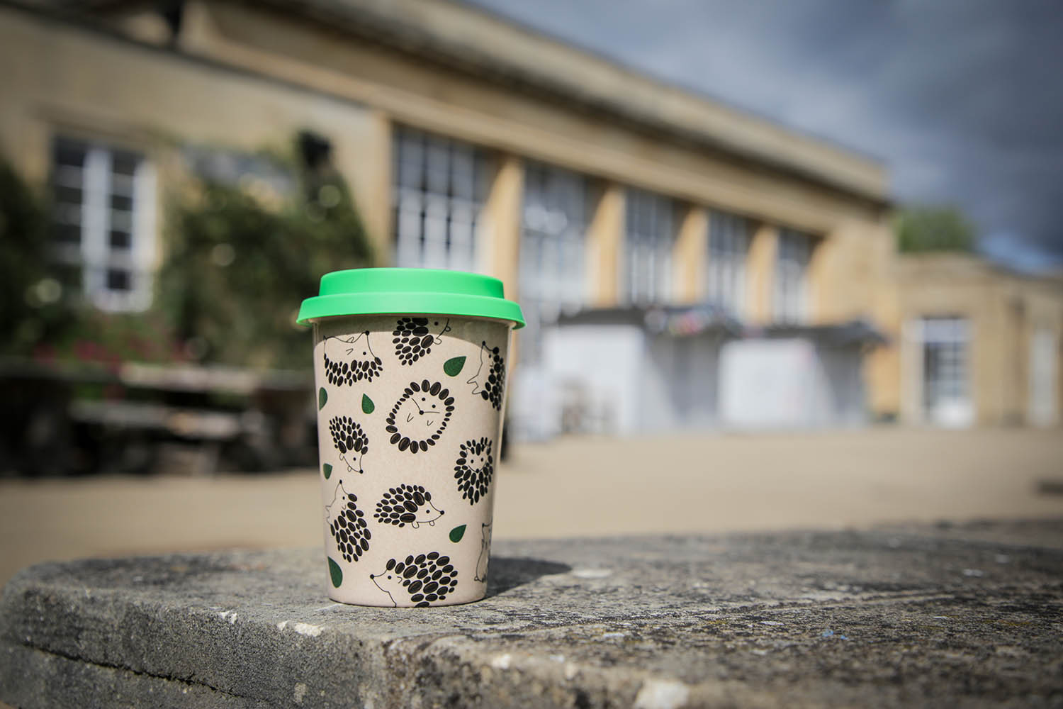A reusable coffee cup with a cute hedgehog motif sitting on a table outside the Refectory.
