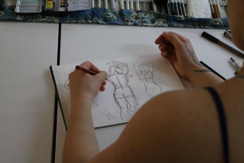 A person sketching a nude model in a notebook
