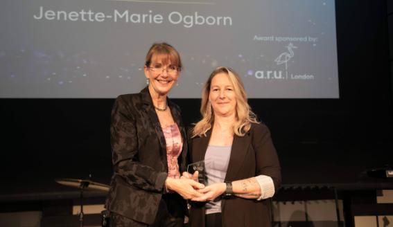 Two women stand together for a photo, holding a trophy
