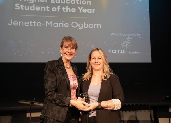 Two women stand together for a photo, holding a trophy between them