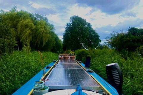 A blue narrowboat sailing down a canal lined by trees.