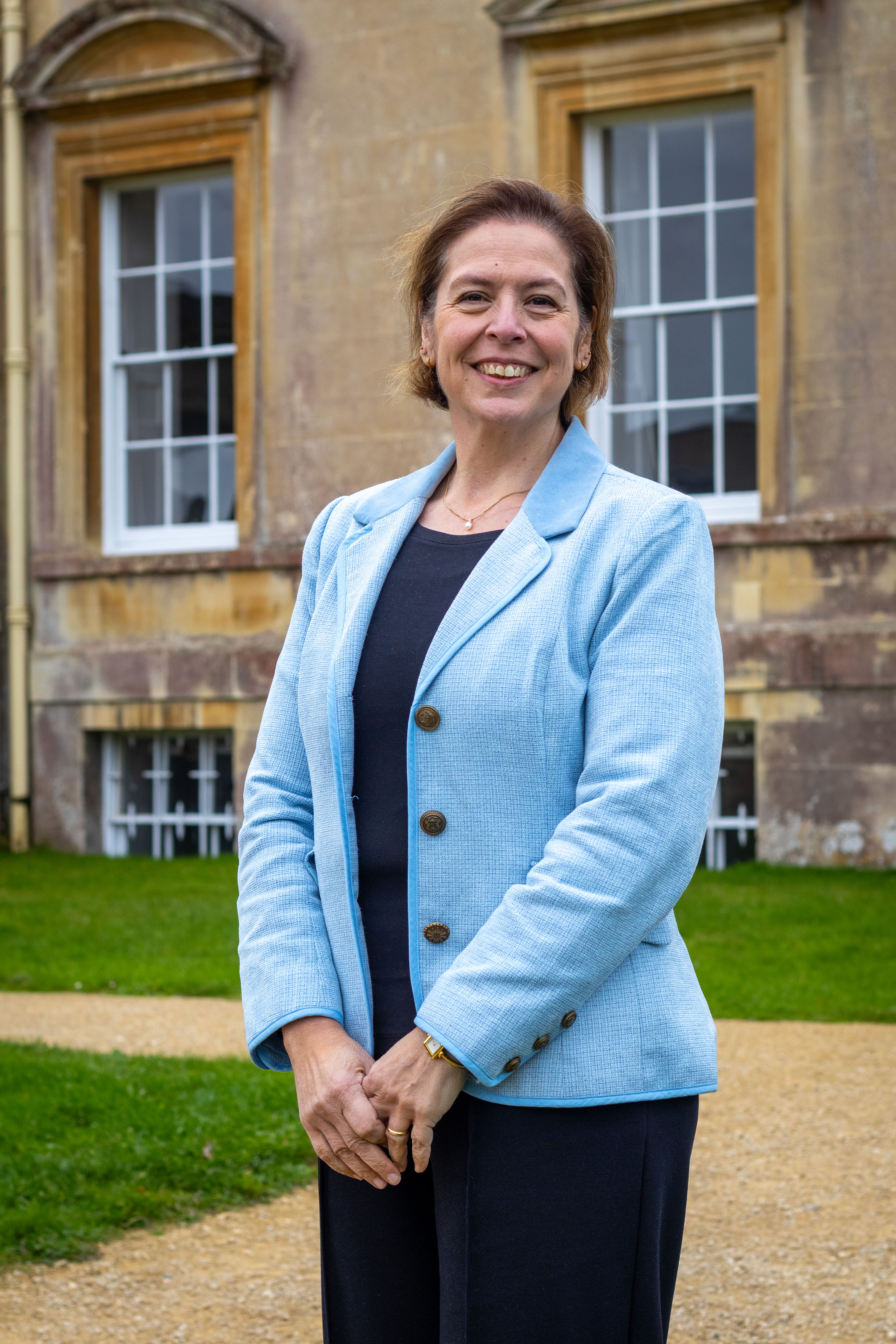 A photo of a woman in a light blue blazer in front of a building