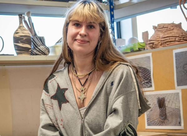 A female student smiling in her studio in front of pottery