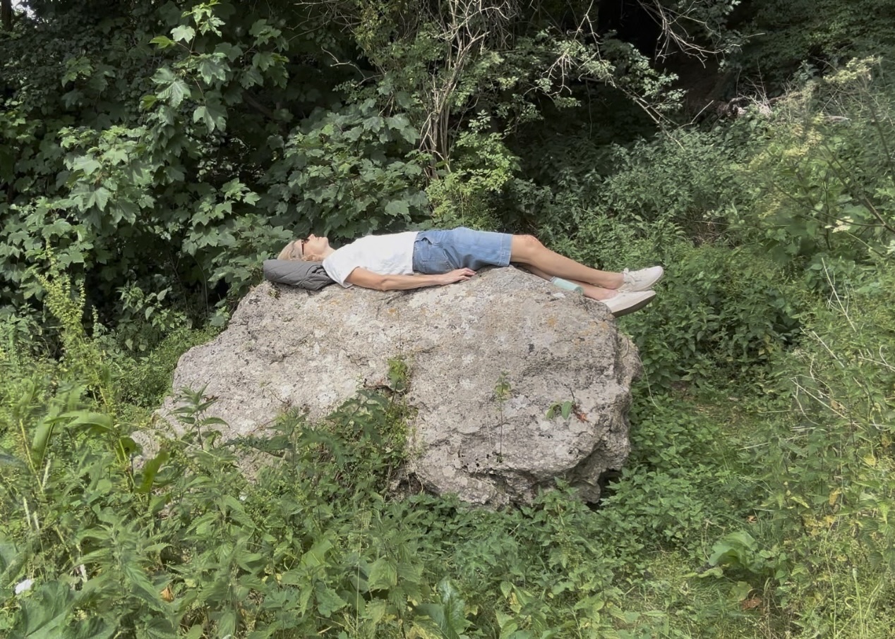 A person lying on a large rock in the woods