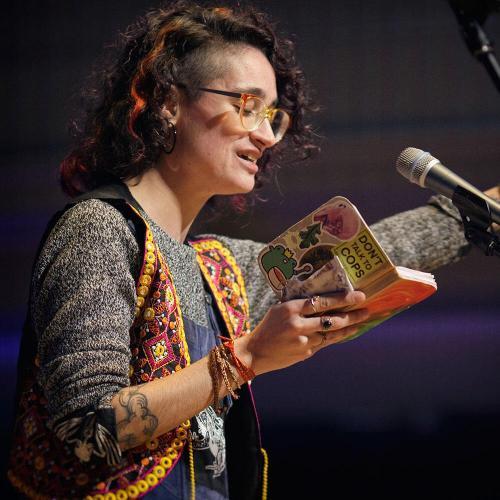 A woman on a mic, reading a poem