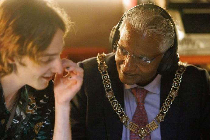 The Mayor of Bath on a set of decks with headphones on, sat next to a student
