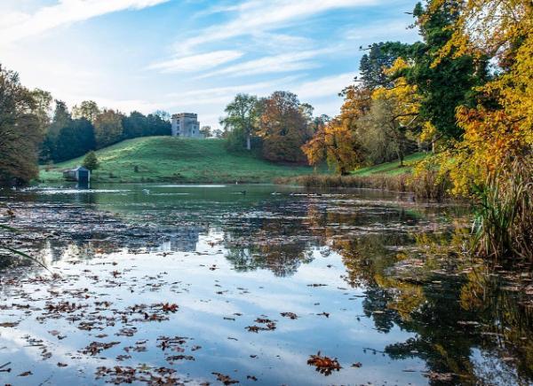 Newton Park lake with blue skies and the castle at the top of the hill