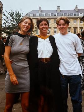 A mother and two children stand smiling in front of a large stone building.